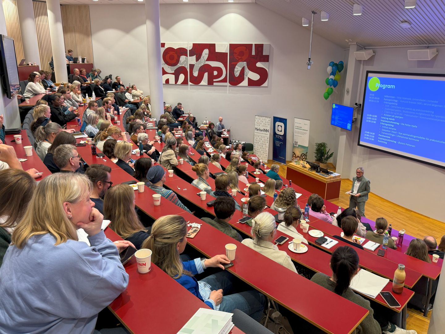 Stor og full forelesningssal med konferansier som ønsker velkommen med dagens program på storskjerm i bakgrunnen
