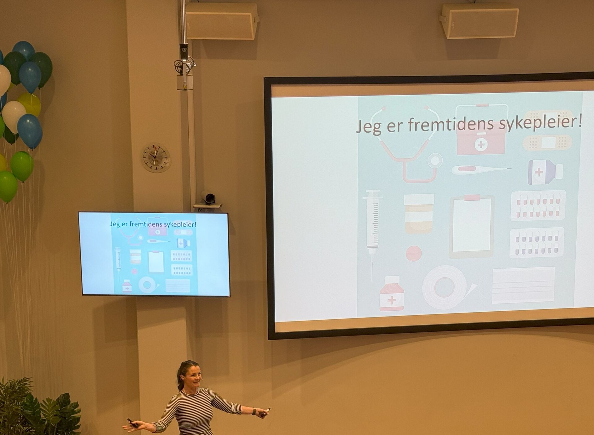 Student holder foredrag for fullsatt forelesningssal. På skjerm i bakgrunnen står det " Jeg er fremtidens sykepleier!"