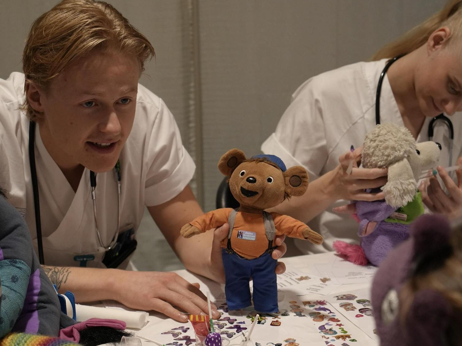 En mannlig og en kvinnelig sykepleierstudent i uniform sitter med hver sin kosebamse. Foto: Barnekreftforeningen.
