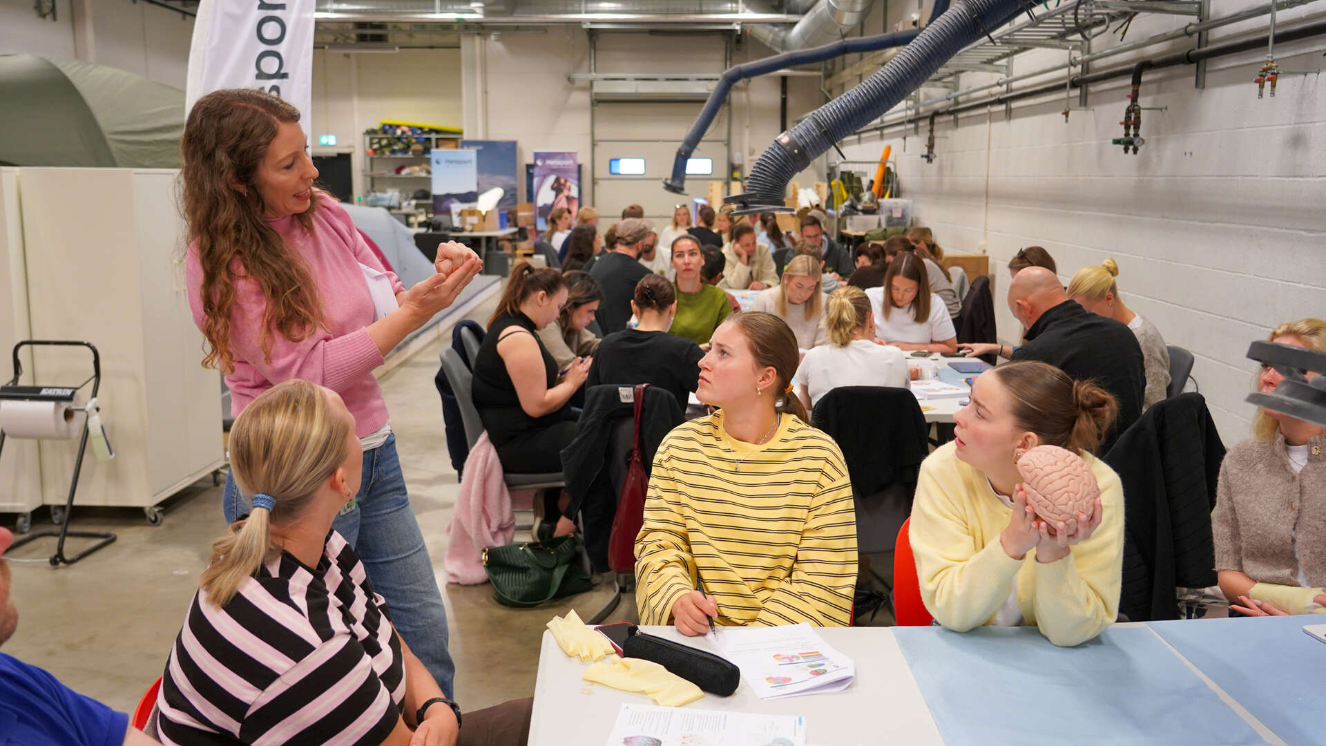 Lærer viser noe foran flere studenter rundt et bord