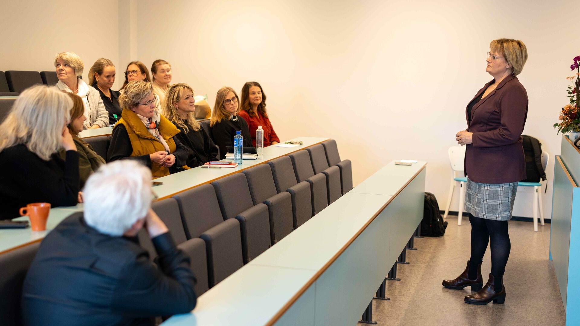 Lucie Furulund står foran og snakker til 11 mennesker i et auditorie.