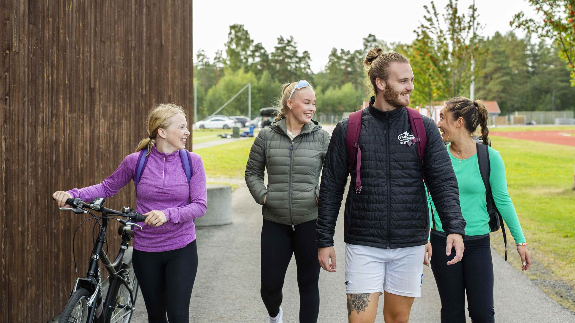 Fire studenter, tre jenter og en gutt i treningstøy utendørs. En har med seg sykkel. Det er god stemning.