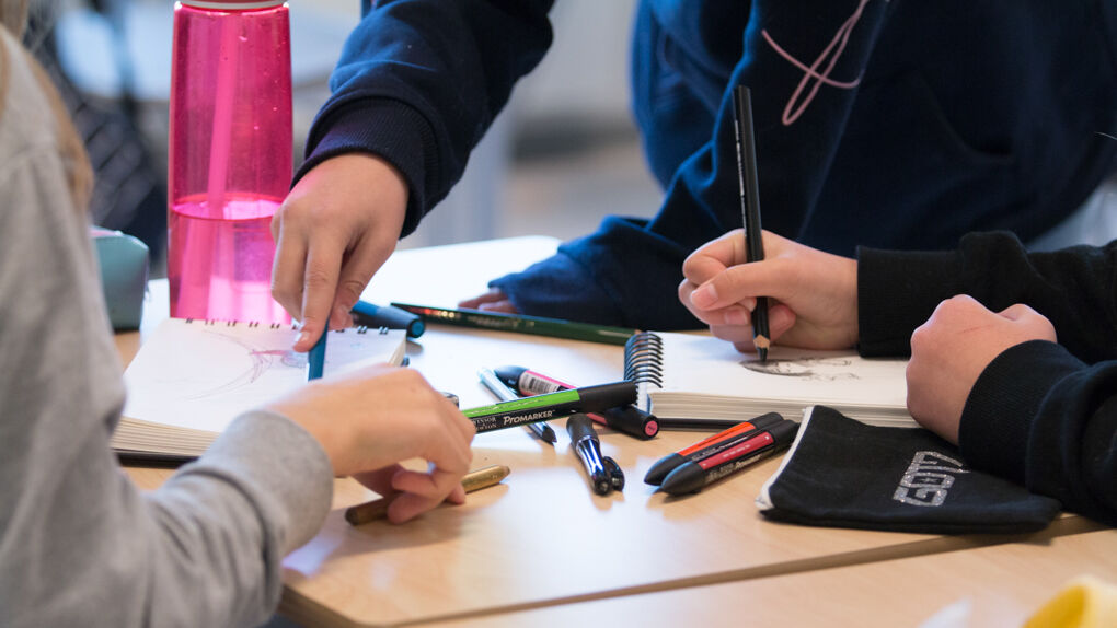 Skolelever rundt et bord med penner og papir