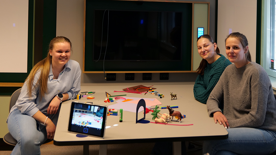 Tre smilende barnehagestudenter som sitter rundt et bord. 