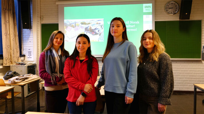 Foto av de fire studentene i et klasserom ved høgskolen