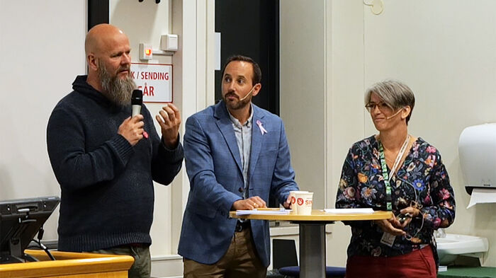 Bilde av de tre paneldeltakerne stående ved kateteret.
