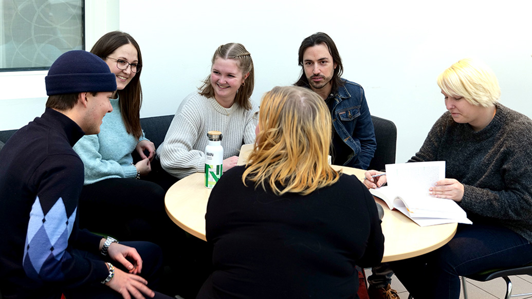 Bilde av seks studenter som sitter rundt et bord og diskuterer.