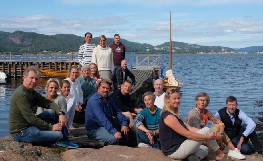 Bilde viser de 17 ansatte samlet på et svaberg og brygge. Blå himmel og sjø i bakgrunnen.