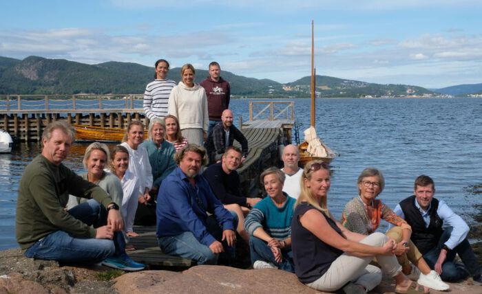 Bilde viser de 17 ansatte samlet på et svaberg og brygge. Blå himmel og sjø i bakgrunnen.