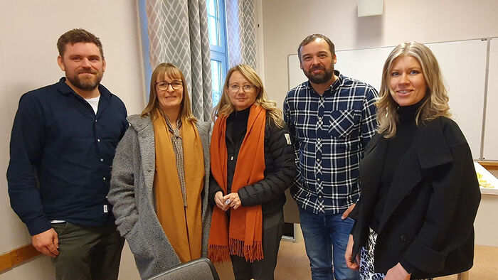 to menn og tre kvinner stiller opp smilende i skolelokale 