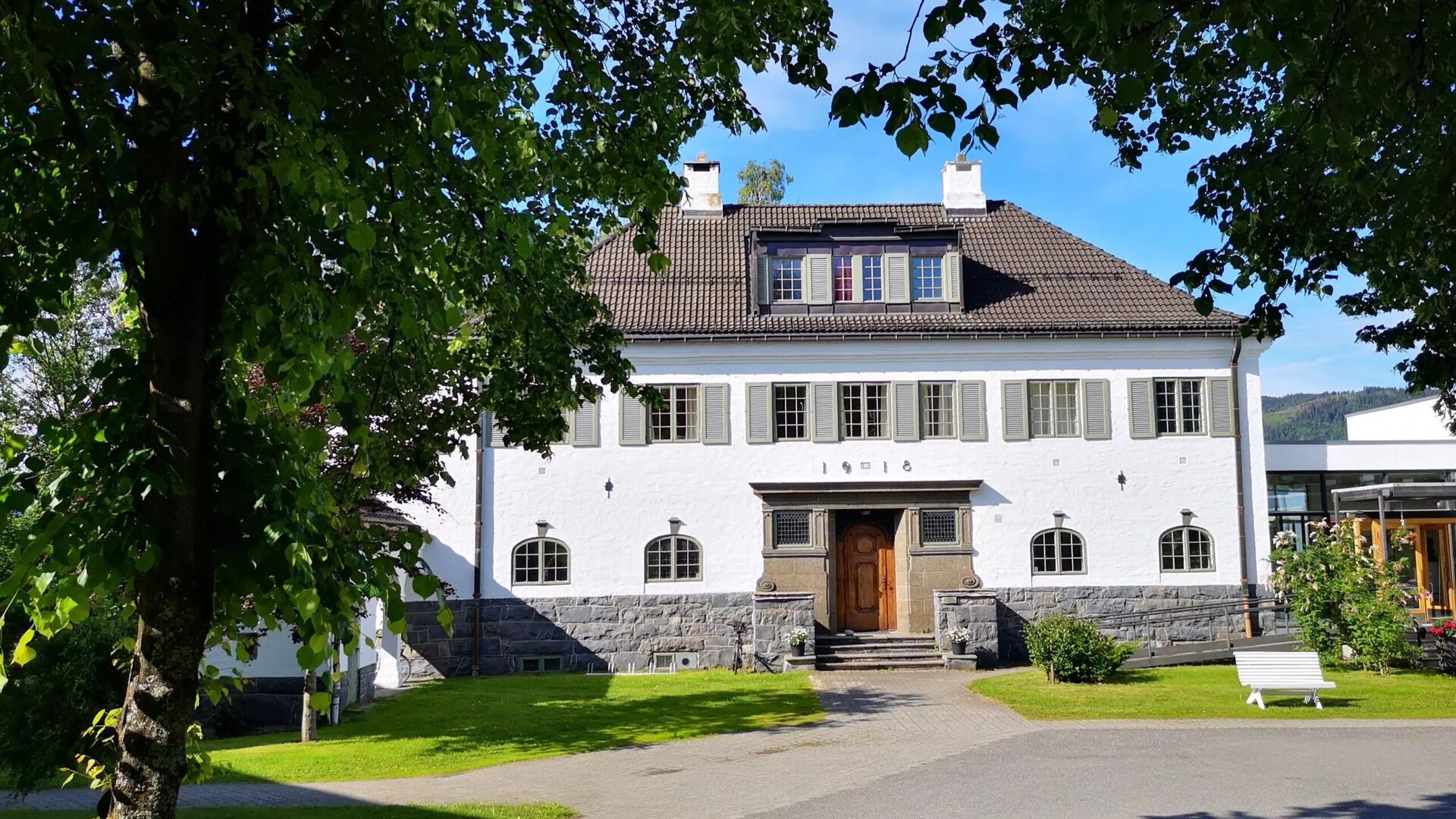 Nansensskolens hvite fasade omringet av grønt bladverk.