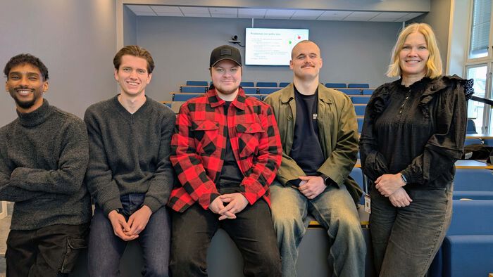 5 studenter oppstilt på rekke i et auditorie. Ser i kamera.