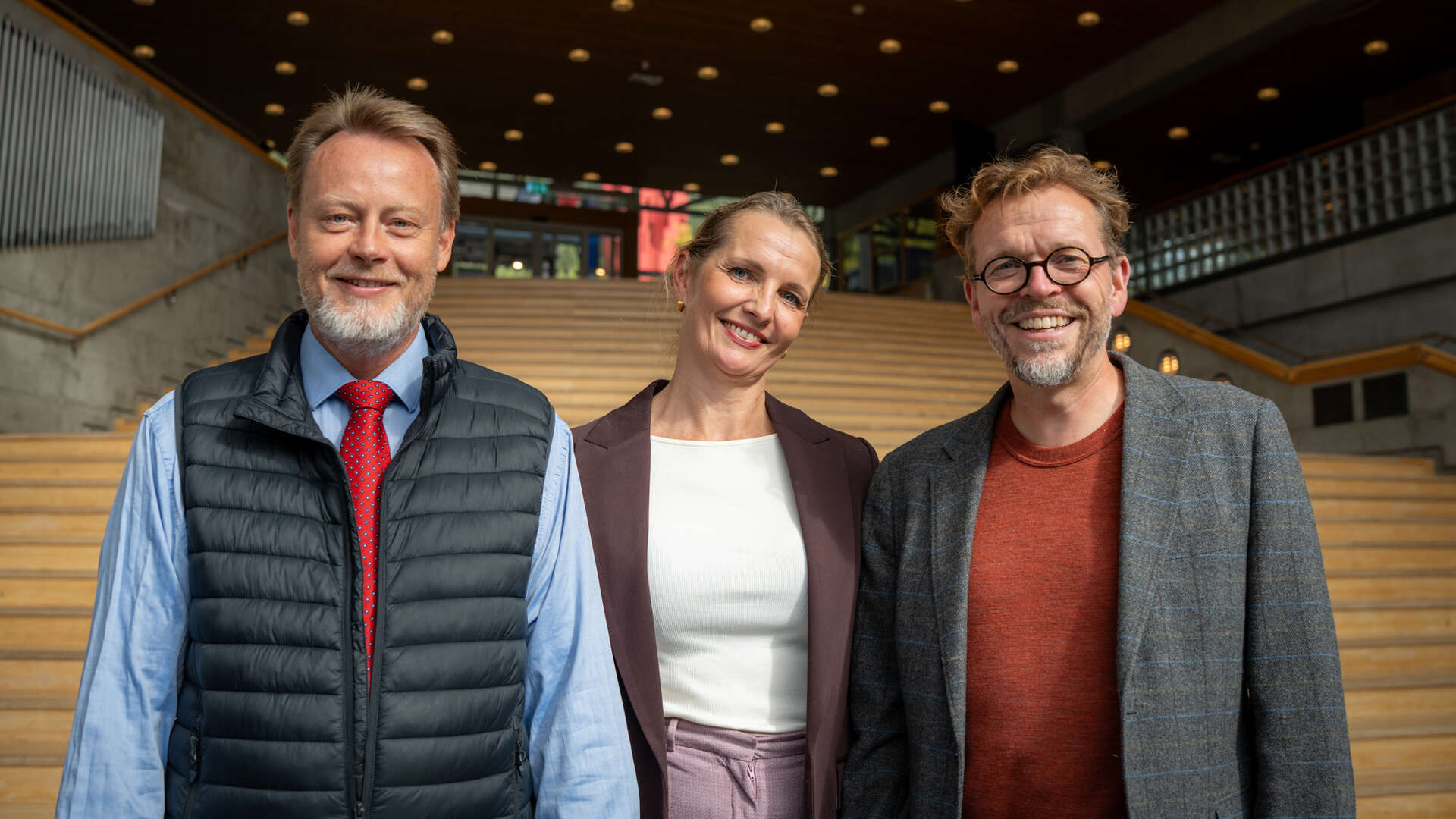 Tre personer står ved siden av hverandre foran en stor trapp