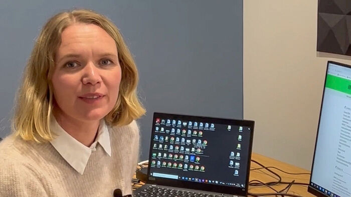 Dame ca 40 smilende foran to pc-skjermer