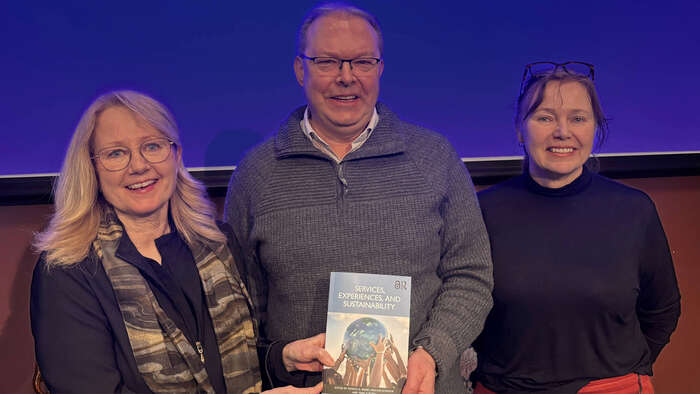 tre personer smiler og holder en bok