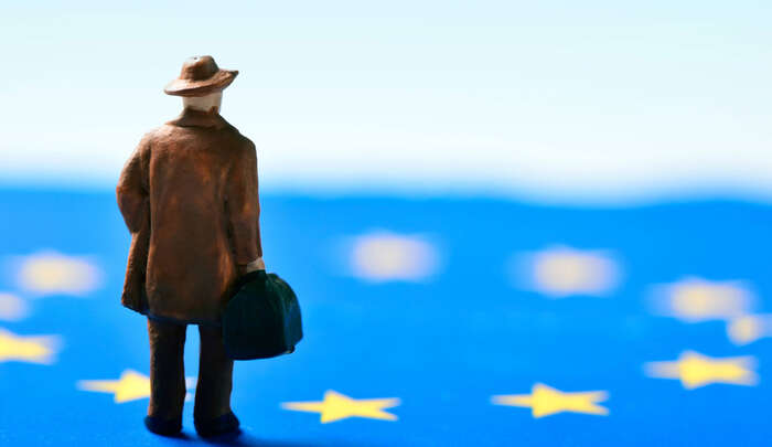 man with hat and suitcase standing on EU flag