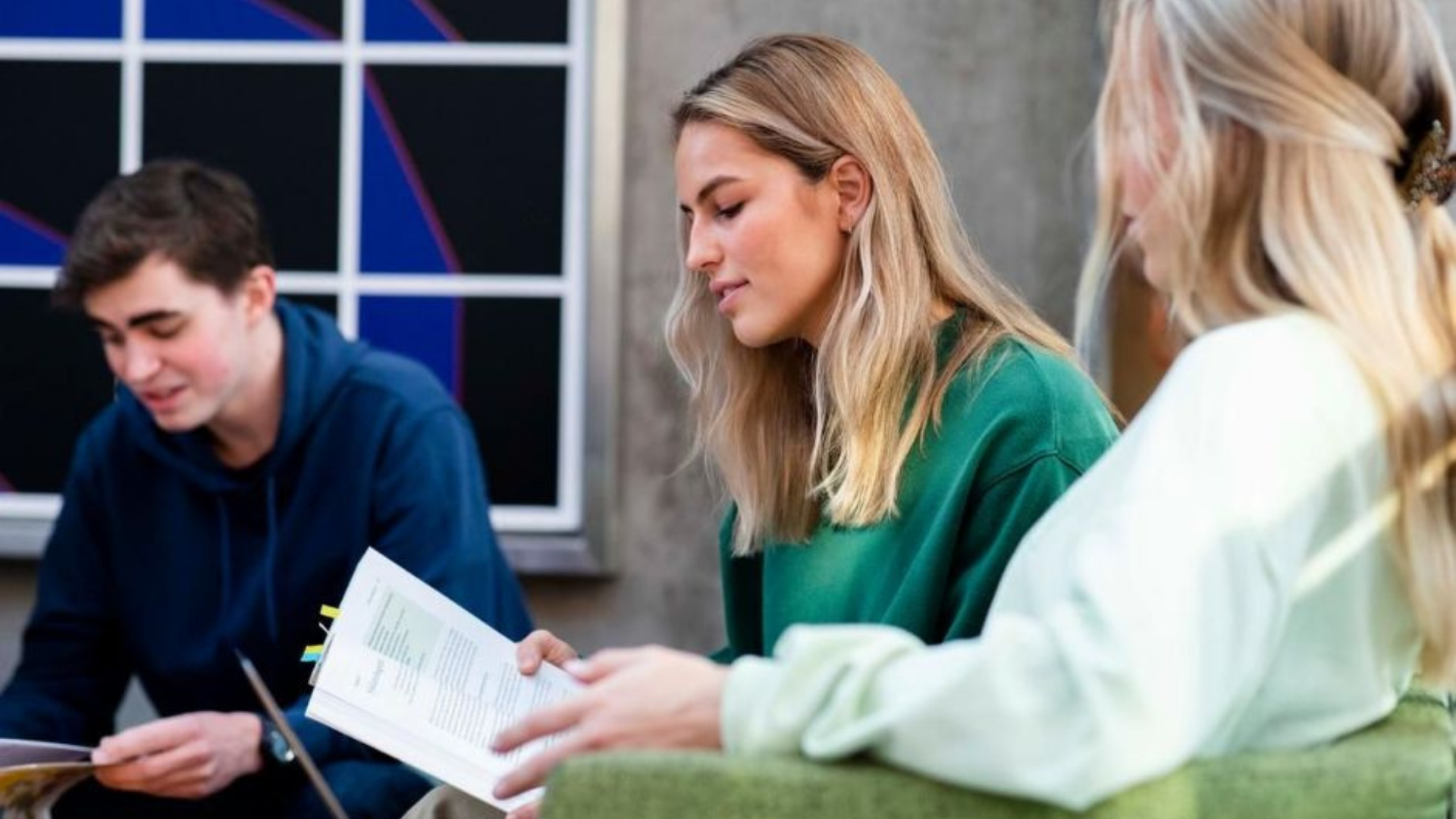 Studenter som sitter å leser sammen, med fokus på ei jente med gronn genser som leser i en bok