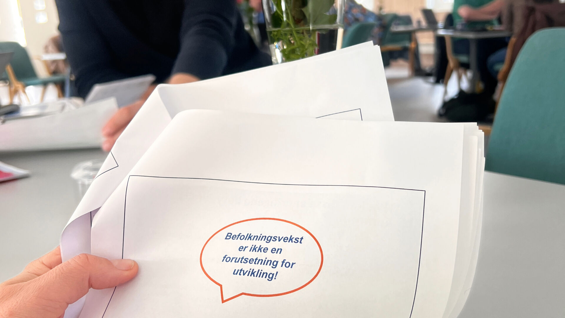 papir med tekst: befolkningsvekst er ikke en forutsetning for utvikling, holdes av en hånd med folk i bakgrunnen