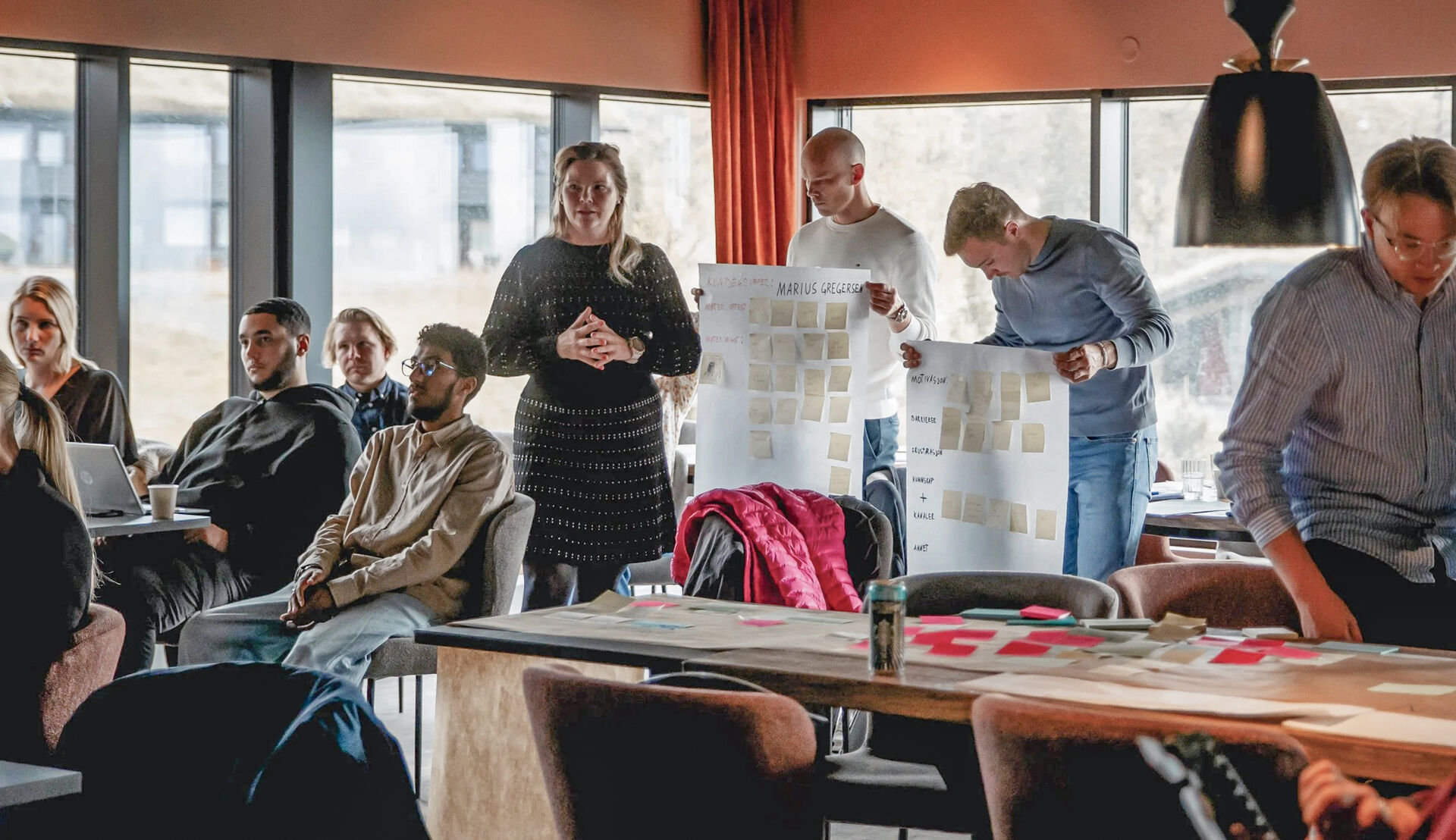 Unge folk står i et rom med gule lapper og store plakater i et arbeidsverksted