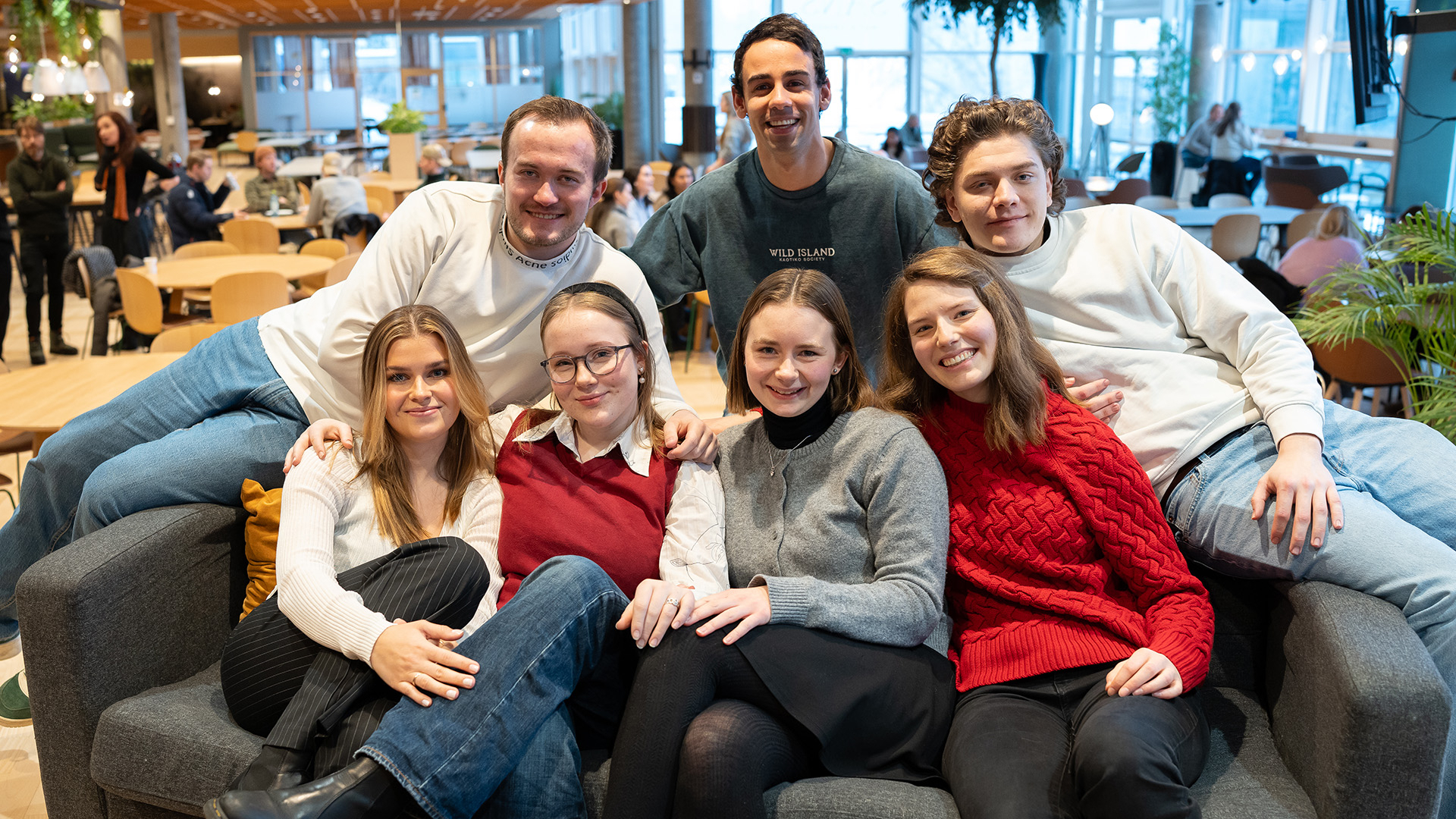 en gjeng på 7 studenter sitter tett og henslengt i en sofa i kantina på Lillehammar.