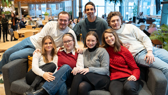 en gjeng på 7 studenter sitter tett og henslengt i en sofa i kantina på Lillehammar.