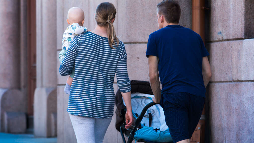 Kvinne med baby på armen, mann triller barnevogn