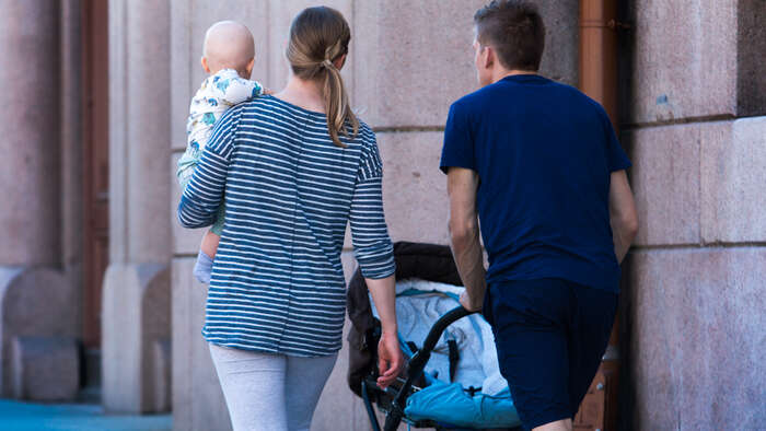 Kvinne med baby på armen, mann triller barnevogn
