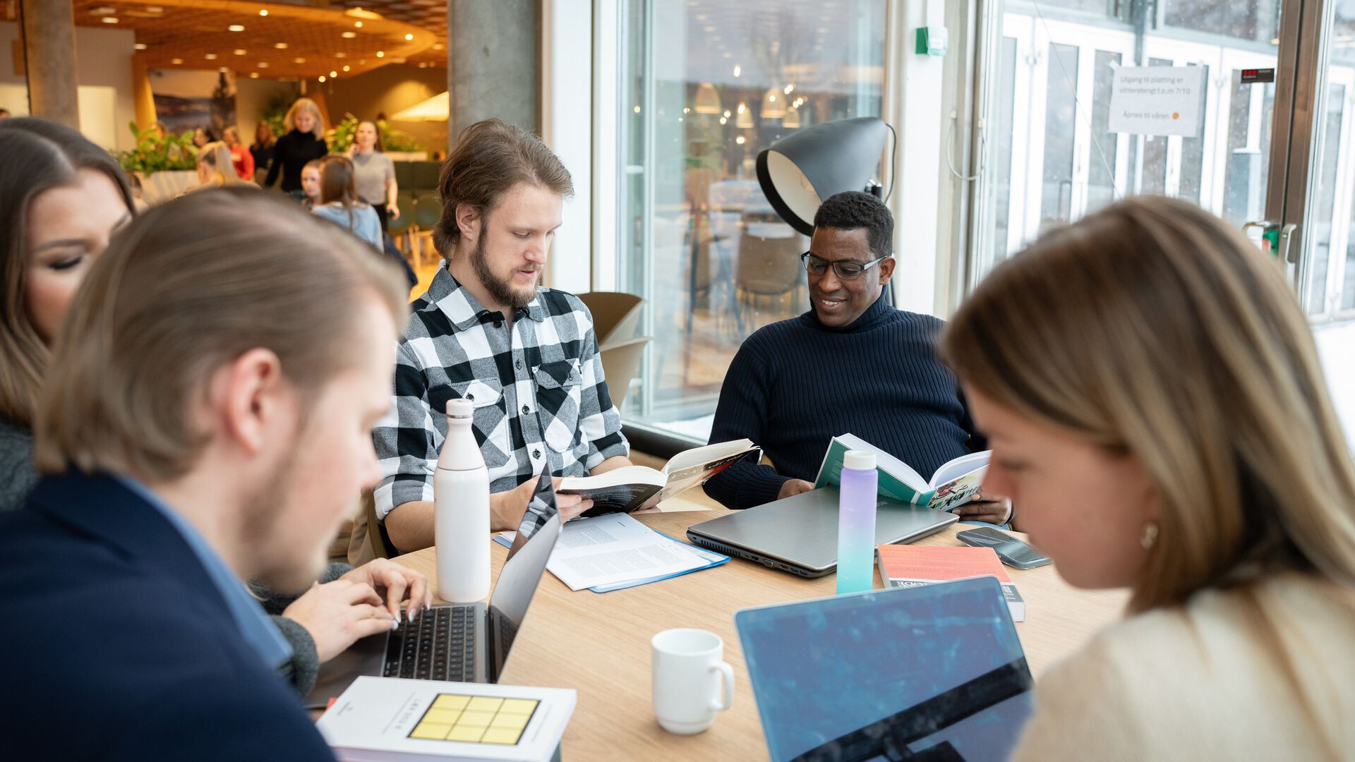 Fem studenter som sitter rundt et bord og ser i lærerbøker