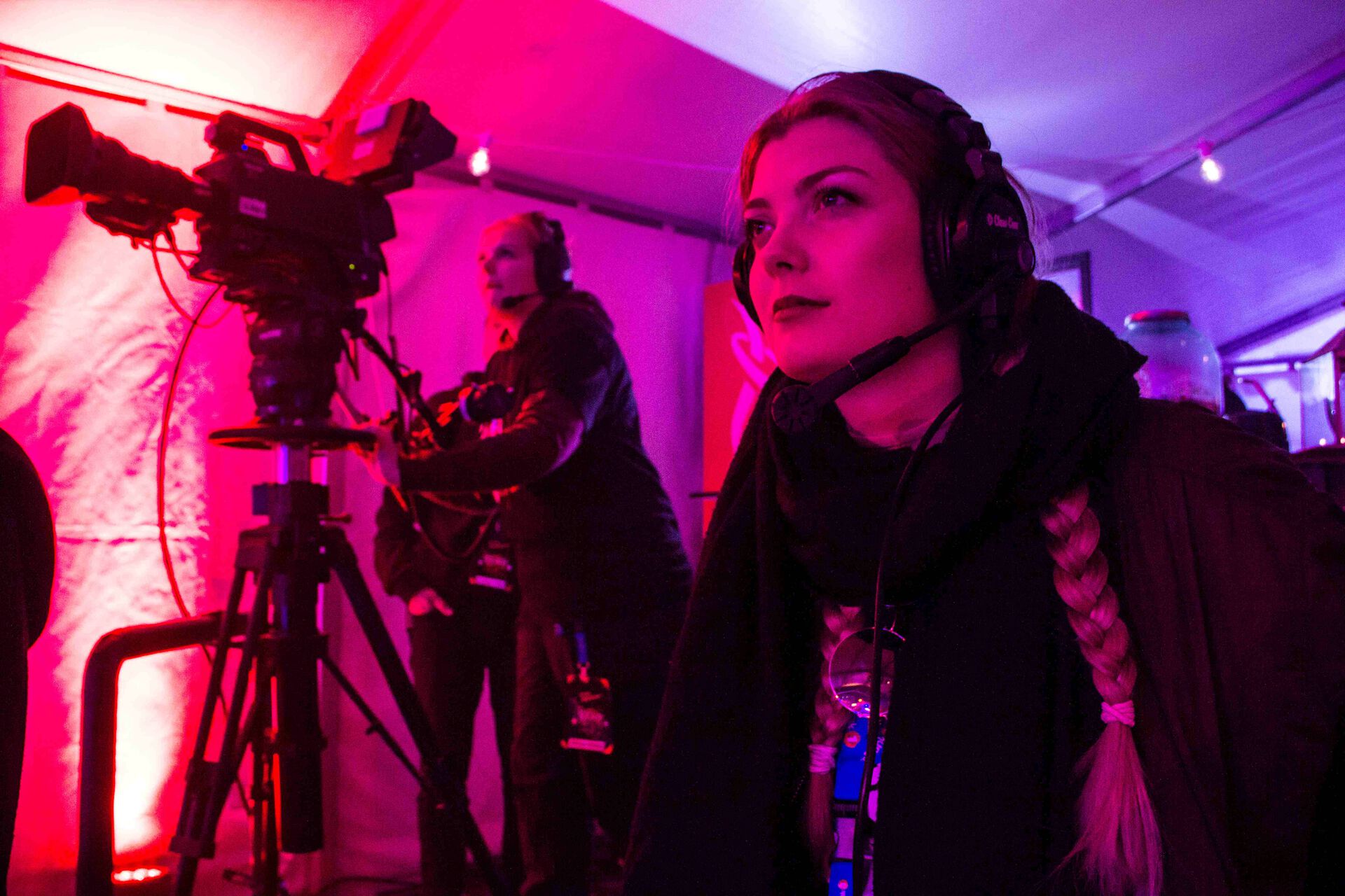 Hele bildet er preget av rødlig lys, to studenter som jobber med filmkamera