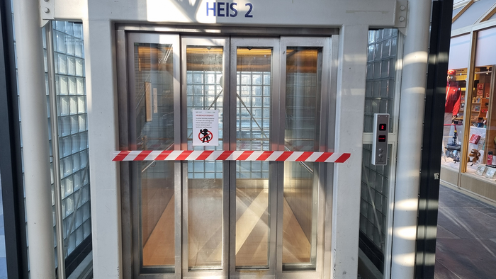 Bildet viser en heis med sperrebånd og en plakat