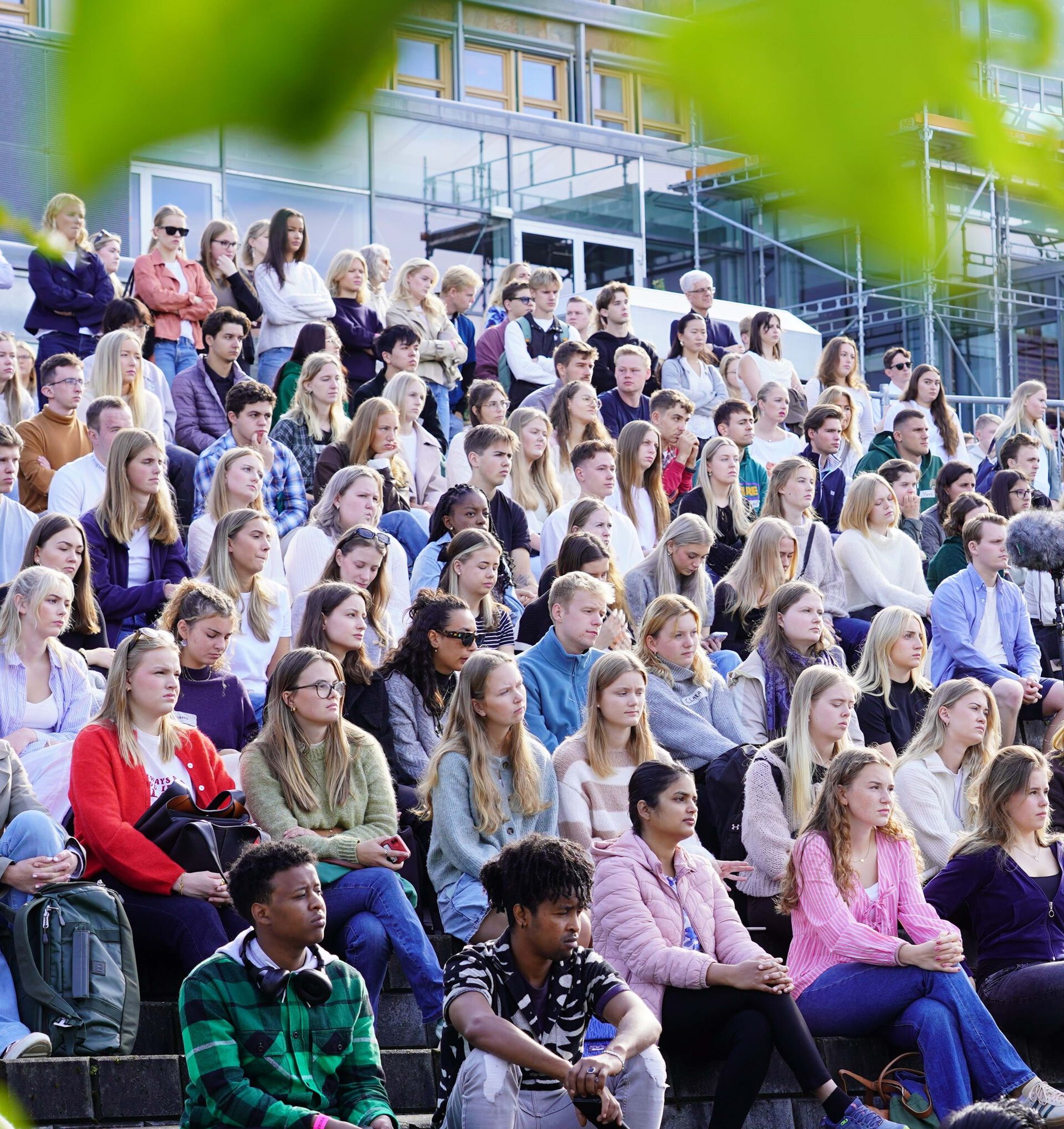 Mange studenter som sitter tett i tett i et amfi ute på studiested Lillehammer ved studiestart, noen grønne blader i forgrunnenn