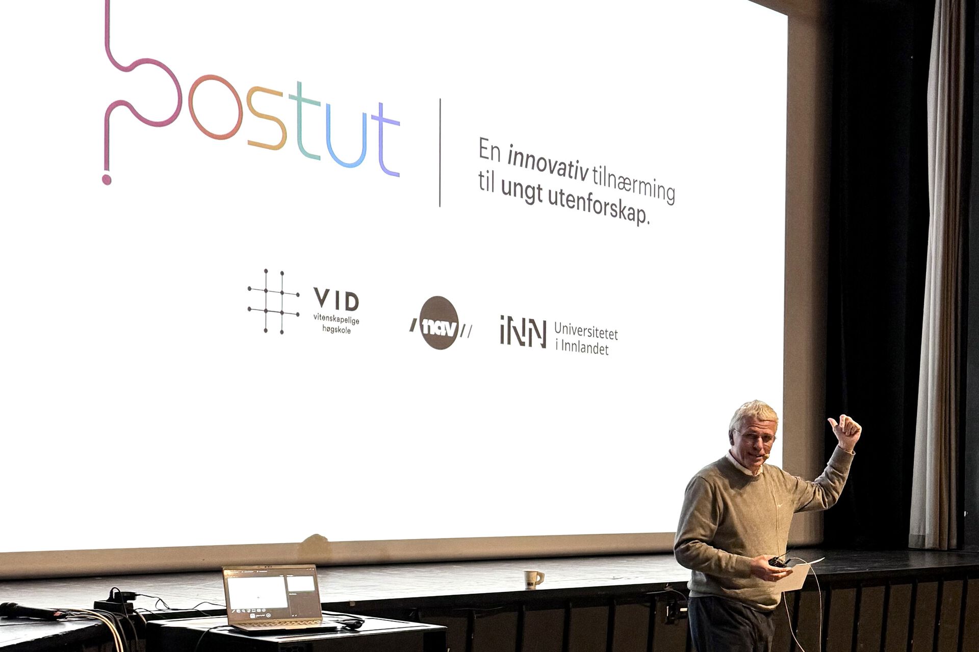 Fylkesdirektør i Nav Innlandet, Bjørn Lien, foran en storskjerm med en presentasjon hvor det står Postut En innovativ tilnærming til ungt utenforskap. Logoene til VID, Nav og INN under.