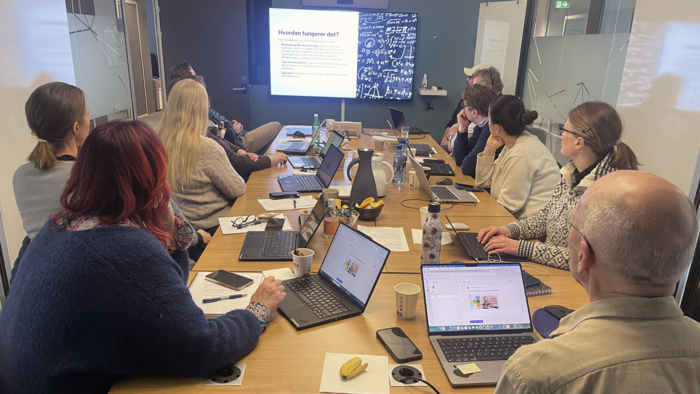 En gruppe studenter som sitter og følger med på et webinar på en storskjerm.