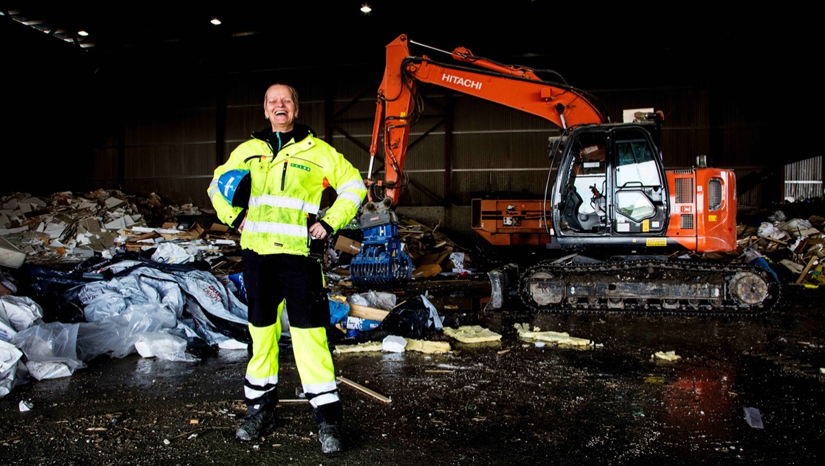 Renovasjonsarbeider står foran gravemaskin og avfall.