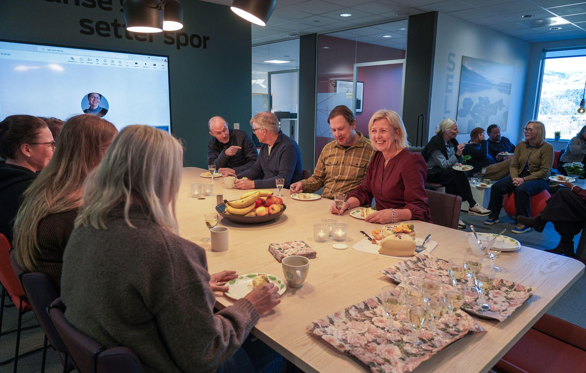 Masse folk som sitter rundt et bord og spiser kake og drikker sjampagne