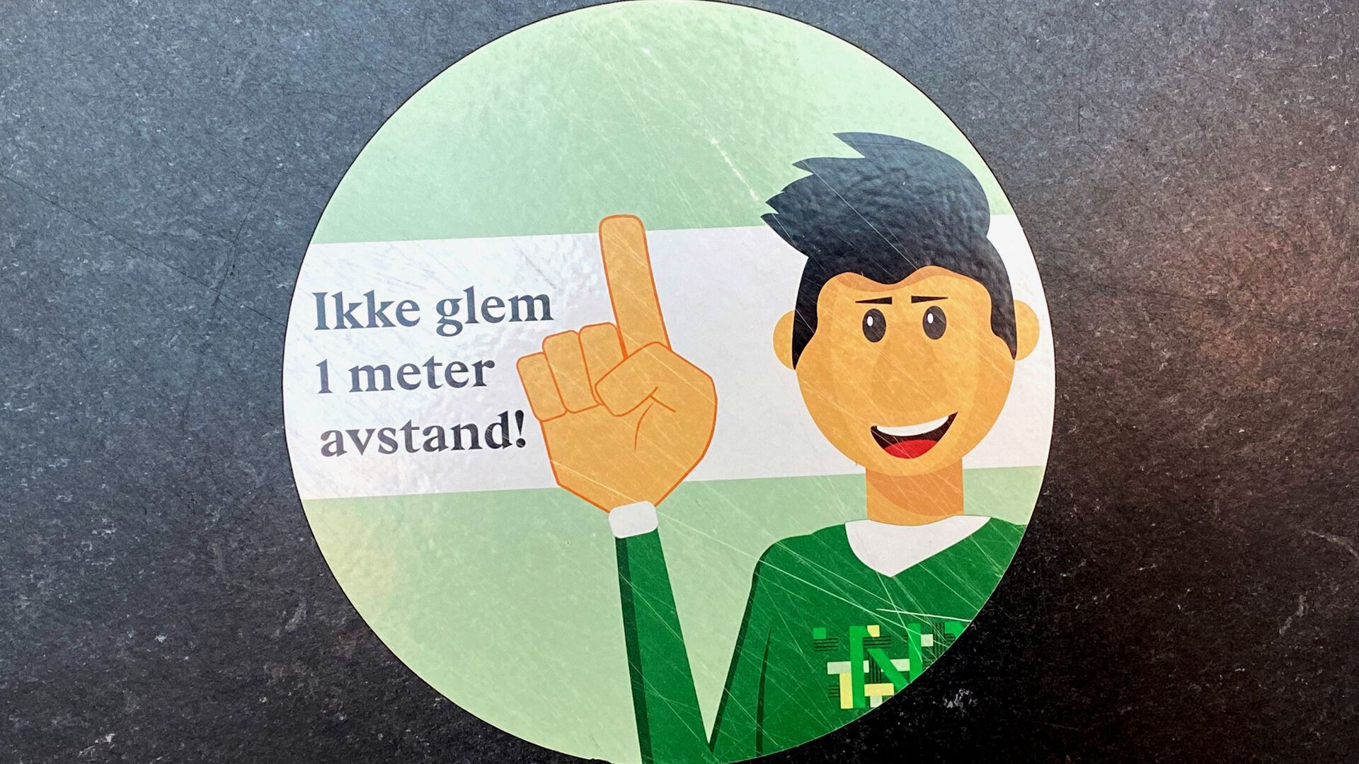 Et klistremerke med teksten "ikke glem en meter avstand" i høgskolens lokaler
