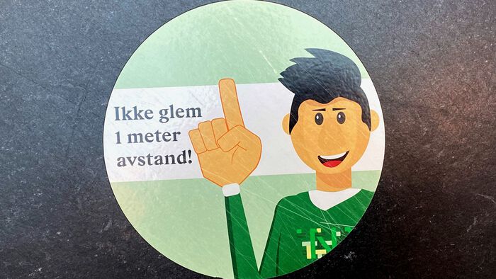Et klistremerke med teksten "ikke glem en meter avstand" i høgskolens lokaler