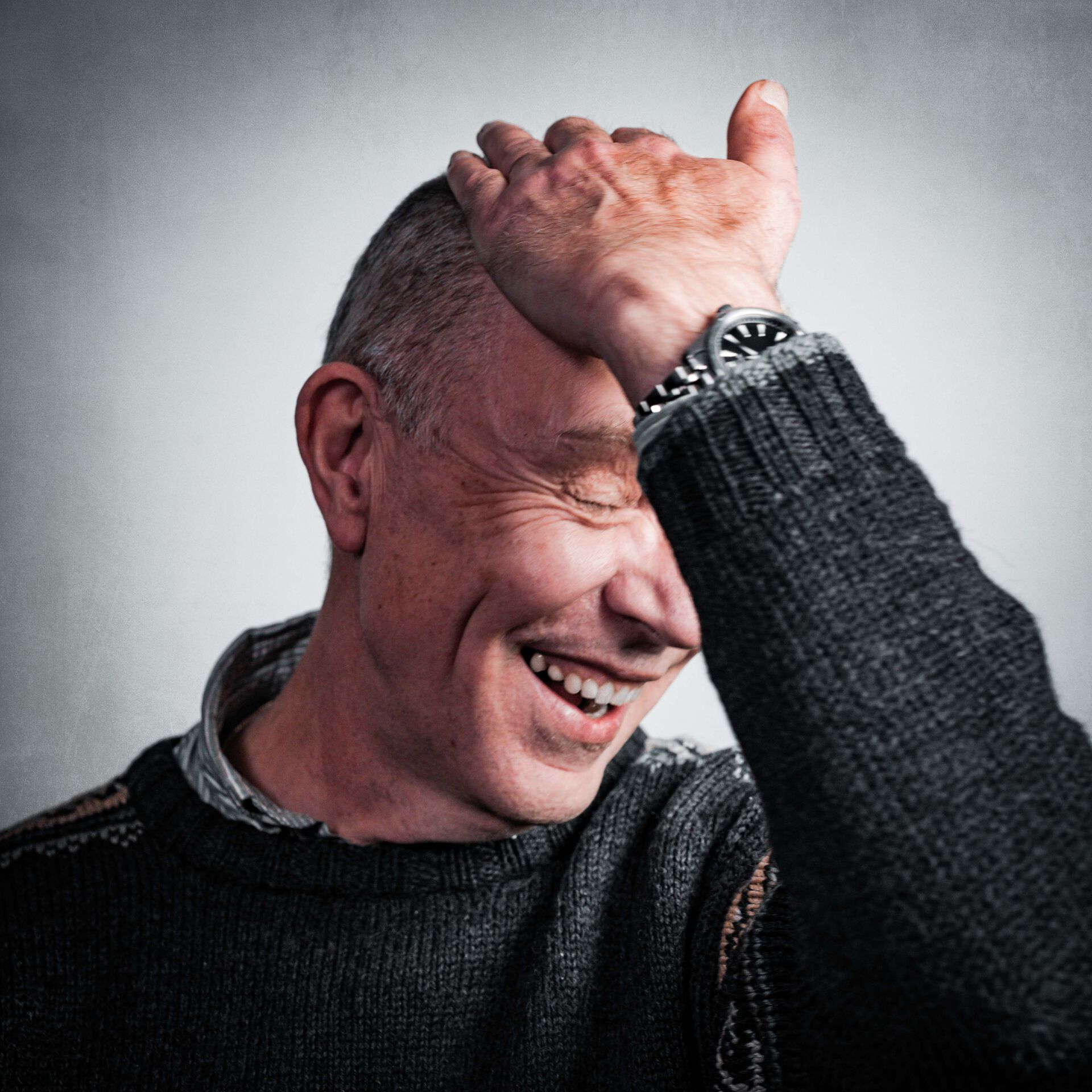 Portrettbilde av Tor Solbakken som ser ned og tar seg til hodet mens han smiler.
