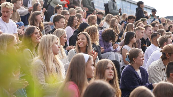 Smilende studenter sitter utendørs i amfiet ved studiested Lillehammer ved studiestart i 2024. Godt vær og god stemning!