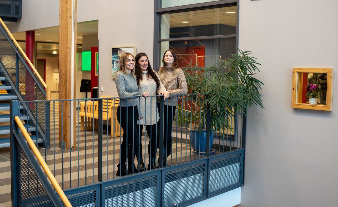 Tre studenter står ved et gelender inne på studiested Rena.