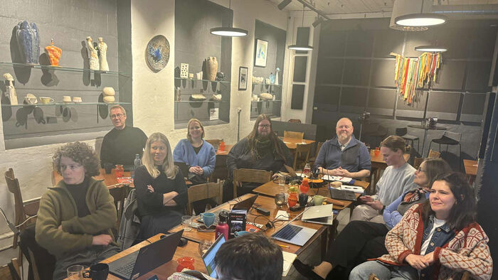 smilende folk rundt et rotete bord med pcer og kaffekopper 