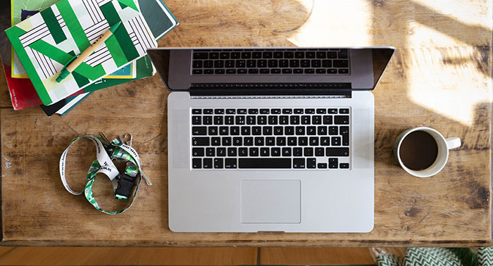 A laptop on a desk is seen from above with INN merch surrounding it
