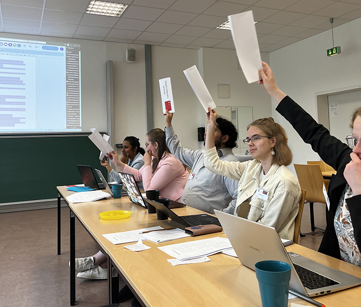 Fem studenter sitter langs et møtebord og avgir stemmer ved å rekke stemmeskilt i været.