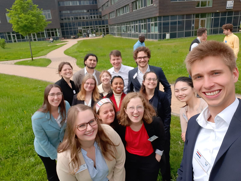 Et gruppebilde av et dusin pent kledde studenter utenfor et campus i Flensburg