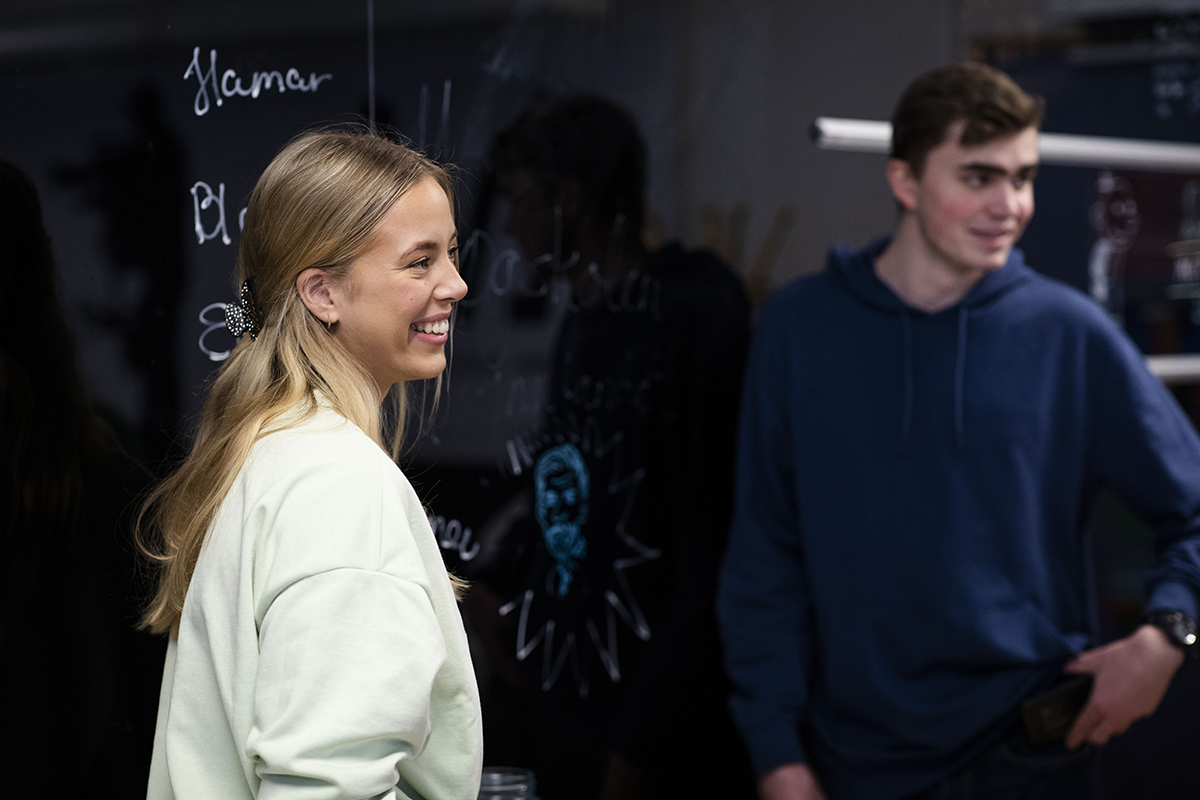 To glade studenter står fremme med tavlen og skuer ut om klasserommet som er utenfor rammen