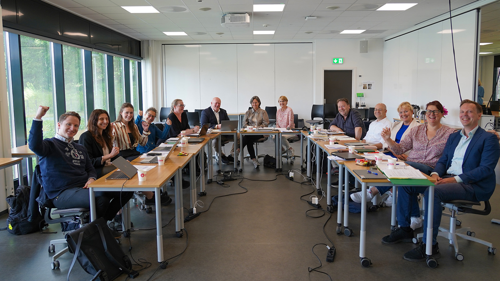 Universitetsstyret samlet rundt et bord i hestesko, og ser glad inn i kamera.