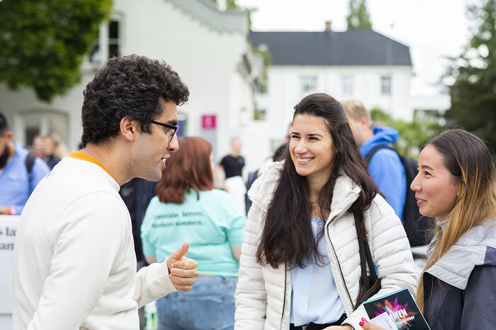 To nye studenter ønskes velkommen av en erfaren student på et utendørs studiestartsarrangement