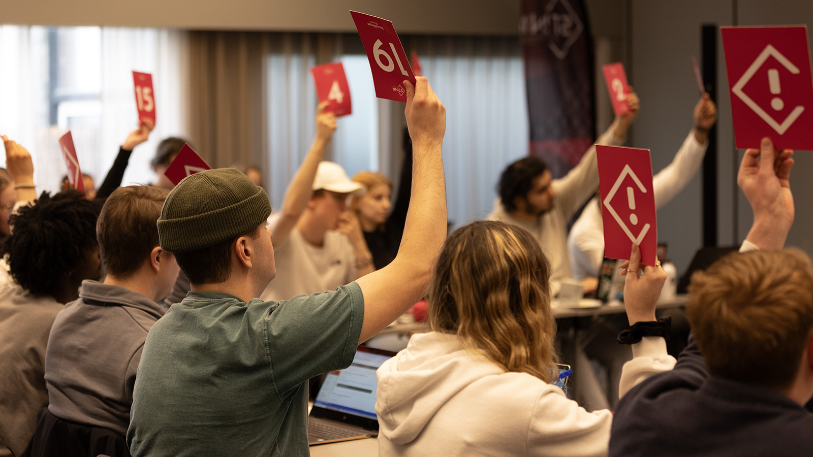 Studentrepresentantene i Studenttinget voterer ved å løfte rosa stemmeskilt med hvite detaljer
