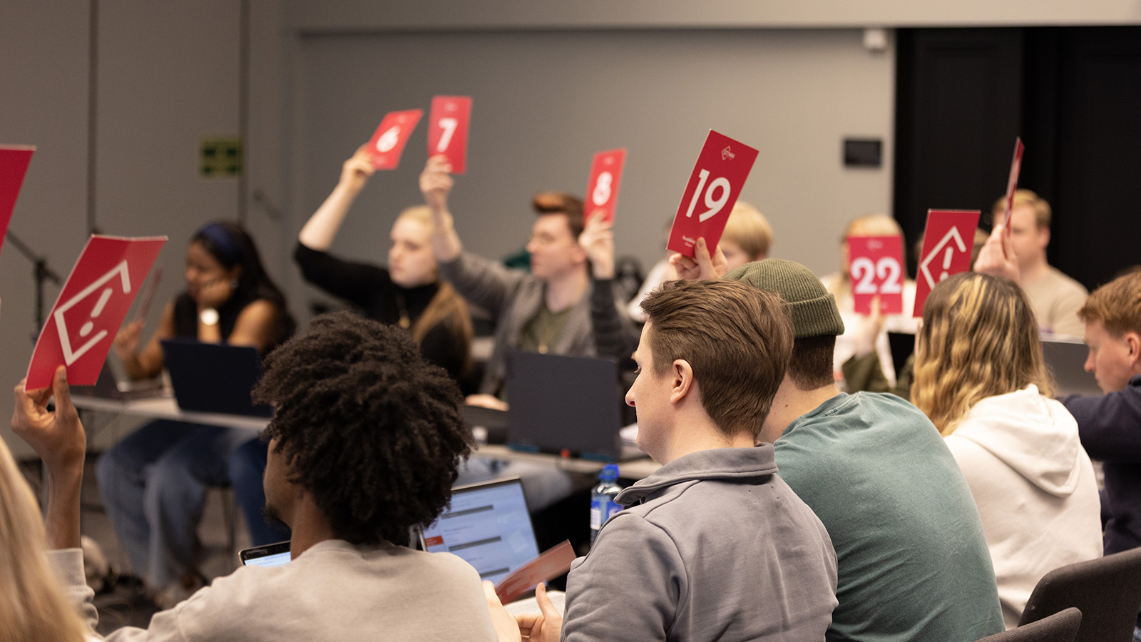 Delegatene i Studenttinget sitter rundt et hesteskoformet bord og voterer ved å løfte stemmeskilt i været.