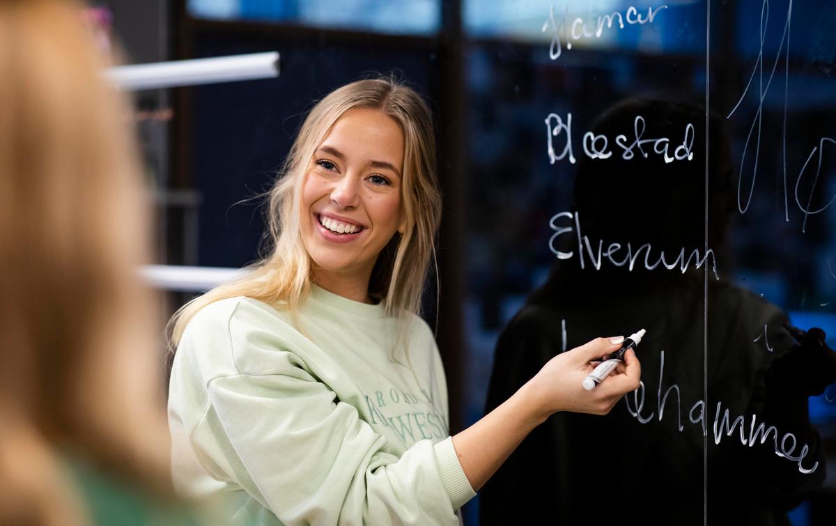 Smilende student foran tavle med navn på studiestedene.